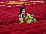 In this photo taken on January 20, 2024 a tourist takes a selfie picture in front of incense sticks arranged in the form of a Vietnamese flag in a courtyard in the village of Quang Phu Cau on the outskirts of Hanoi. Families living and working in the "incense village" of Quang Phu Cau now also make sticks in yellow, blue and green, catering to visitors eager to snap shots for Instagram. 