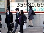 People walk in front of an electronic stock board.