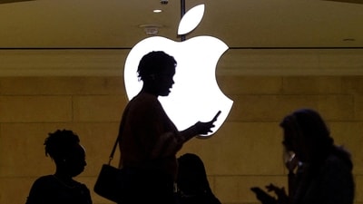 A women uses an iPhone mobile device as she passes a lighted Apple logo at the Apple store (REUTERS)