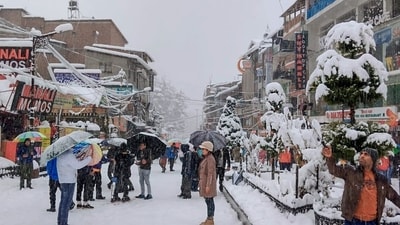 Tourists cover their heads with umbrellas as they enjoy snowfall at Mall Road, in Shimla on Thursday. (ANI)