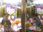 The image shows a 3-year-old kid stuck inside a Hello Kitty claw machine. The image shows a 3-year-old kid stuck inside a Hello Kitty claw machine.