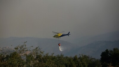 A helicopter flying over a burnt area drops water from a bucket to douse flames during the spread of wildfires in Vina del Mar, Chile. (REUTERS)