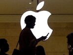 A women uses an iPhone mobile device as she passes a lighted Apple logo at the Apple store