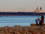 People walk on the beach as a container ship crosses the Gulf of Suez towards the Red Sea before entering the Suez Canal.