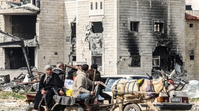 Palestinians ride a donkey-pulled cart past the ruins of a building in the Maghazi camp for Palestinian refugees. (AFP)