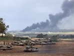 Israel-Hamas War: Israeli soldiers stand next to tanks at a position in Israel near the border with the Gaza Strip as smoke billows over the Gaza Strip after Israeli bombardment.
