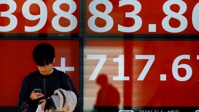 A man uses his smartphone in front of an electronic screen displaying Japan's Nikkei share average as the share average climbed to a record high outside a brokerage in Tokyo, Japan. (Reuters)