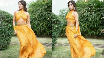 Bhumi's Punit Balana Bandhani print outfit features a sleeveless cropped blouse. It has a halter neckline, a train on the back, an asymmetric hem exposing her toned midriff, gold sequin embellishments, and a fitted silhouette. Meanwhile, the Bandhani lehenga skirt has a high-rise waist, a sequin embellished gota patti belt, a flowy silhouette, a pleated front, and a floor-length asymmetric hem.&nbsp; (Instagram)