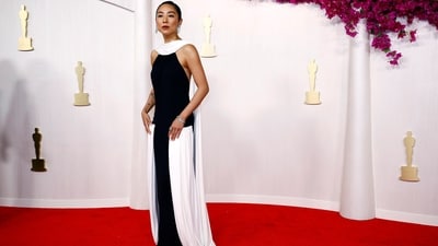 Greta Lee debuted at the Academy Awards in an incredible black velvet halter neck gown by Loewe featuring a gorgeous backless design. The dress had gauzy white strips of fabric draped across her neck and down her back, attached to the front of her hips. Diamond-encrusted paper-clip earrings, bracelets, rings, a side-parted sleek bun, and cherry lips glammed up her attire.&nbsp; (REUTERS)
