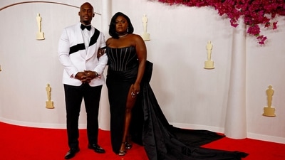 Danielle Brooks and a guest pose on the red carpet during the Oscars 2024 in Hollywood, Los Angeles. She arrived in a bedazzled jersey coat dress by Dolce &amp; Gabbana featuring a thigh-high slit, embellished corset, and a bow train on the back.&nbsp; (REUTERS)