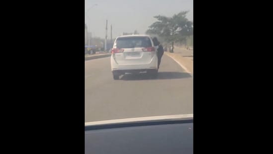 Snapshot of the woman hanging from moving car's door. (X/@Vivek K. Tripathi)