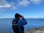 A coast guard officer looking through binoculars as a drone searches for victims