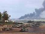 Israel-Hamas War: Israeli soldiers stand next to tanks at a position in Israel near the border with the Gaza Strip as smoke billows over the Gaza Strip after Israeli bombardment.
