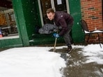 Mikey Reynolds, an employee at The Works on Main Street in Brattleboro, Vt., shovels the sidewalk in front of the restaurant as a person who is facing homelessness sleeps in a door entryway while seeking refuge from the snow storm on Saturday, March 23, 2024. New England is battling a mix of wind, rain, sleet and heavy snow across the region Saturday with more than a foot of snow expected in ski county, but mostly rain, wind and possible flooding in southern areas and along the coast.  (Kristopher Radder  /The Brattleboro Reformer via AP)