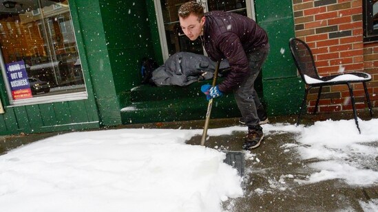Mikey Reynolds, an employee at The Works on Main Street in Brattleboro, Vt., shovels the sidewalk in front of the restaurant as a person who is facing homelessness sleeps in a door entryway while seeking refuge from the snow storm on Saturday, March 23, 2024. New England is battling a mix of wind, rain, sleet and heavy snow across the region Saturday with more than a foot of snow expected in ski county, but mostly rain, wind and possible flooding in southern areas and along the coast. (Kristopher Radder /The Brattleboro Reformer via AP) (AP)