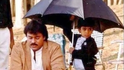 A young Ram holds an umbrella as his father Chiranjeevi sits outdoors during a shoot on sets of a film. A young Ram holds an umbrella as his father Chiranjeevi sits outdoors during a shoot on sets of a film. 