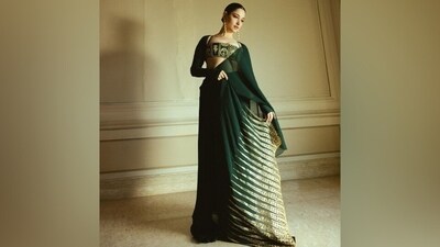 Celebrity stylist Leepakshi Ellawadi styled Masaba in the ethnic yet modern ensemble. The dark green georgette, pre-draped saree comes embellished with a Trikone embroidery done on the palla with gold dori and sequin work. The sheer drape features a floor-sweeping pallu, pleats on the side, a ruffled train attached on the hip, and a figure-hugging pre-draped silhouette. (Instagram) Celebrity stylist Leepakshi Ellawadi styled Masaba in the ethnic yet modern ensemble. The dark green georgette, pre-draped saree comes embellished with a Trikone embroidery done on the palla with gold dori and sequin work. The sheer drape features a floor-sweeping pallu, pleats on the side, a ruffled train attached on the hip, and a figure-hugging pre-draped silhouette. (Instagram)