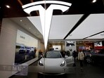 Visitors check a Tesla Model 3 car next to a Model Y displayed at a showroom.