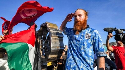 People wave Palestinian and Tunisian flags while British runner Russ Cook gestures as he poses for a picture with the memorial sign marking the northern-most point of Africa (AFP) People wave Palestinian and Tunisian flags while British runner Russ Cook gestures as he poses for a picture with the memorial sign marking the northern-most point of Africa (AFP)