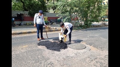 Gurugram traffic police personnel repairing potholes on Old MG Road in Gurugram on Friday. (Parveen Kumar/HT PHOTO)