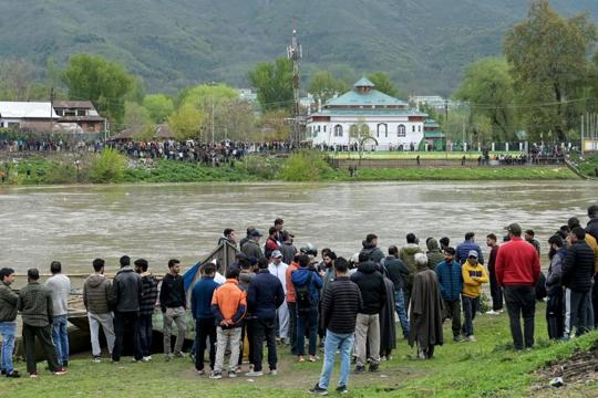 People gather along the Jhelum riverside as National Disaster Response Force (NDRF) personnel conduct a search and rescue operation after a boat with children overturned in Srinagar on Tuesday. (AFP Photo) People gather along the Jhelum riverside as National Disaster Response Force (NDRF) personnel conduct a search and rescue operation after a boat with children overturned in Srinagar on Tuesday. (AFP Photo)