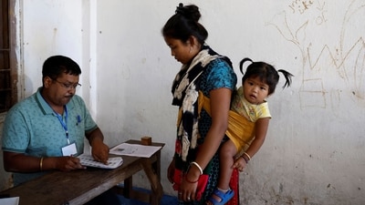 A woman from the Toto tribe, carrying her daughter, gets her name checked in a voters list at a polling station in Alipurduar district, West Bengal. (Sahiba Chawdhary  / Reuters)