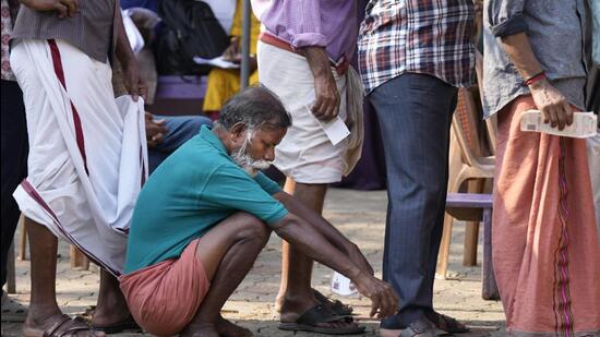 A man squats to rest as people queue up to vote during the second round of voting near Palakkad (AP)