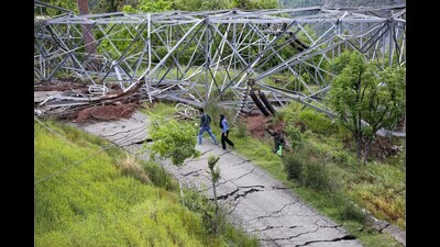 People walk past a fallen electric tower on a cracked road in Ramban district on Saturday. (PTI) People walk past a fallen electric tower on a cracked road in Ramban district on Saturday. (PTI)