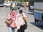 Women, covering their faces, walk amid sweltering heat.