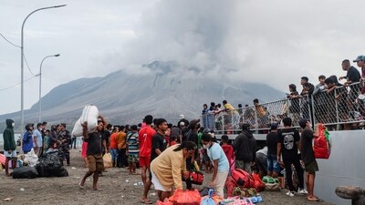 Evacuees board an Indonesian naval vessel on Tagulandang Island in Sitaro, North Sulawesi as Mount Ruang volcano spews smoke in the background. (AFP)