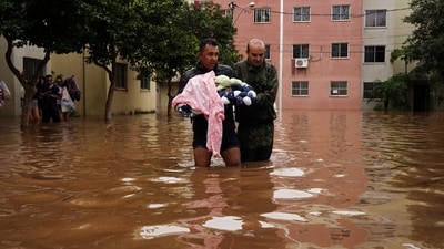 A man, carrying a baby, wades through a street flooded by heavy rains, in Canoas, Rio Grande do Sul state, Brazil. (AP) A man, carrying a baby, wades through a street flooded by heavy rains, in Canoas, Rio Grande do Sul state, Brazil. (AP)