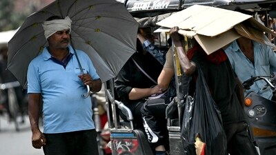 A man (L) takes shelter under an umbrella from the scorching sun on a hot summer afternoon (AFP)