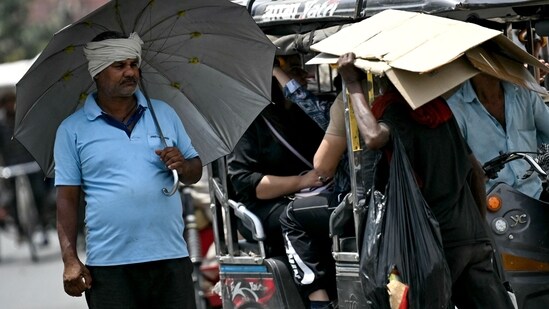 A man (L) takes shelter under an umbrella from the scorching sun on a hot summer afternoon (AFP)