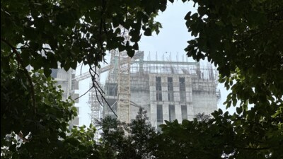 An upcoming hospital building is seen through foliage of two roadside peepal trees on Asaf Ali Marg. (HT Photo)