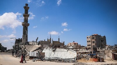 People walk past a destroyed warehouse in Khan Yunis in the southern Gaza Strip. (AFP) People walk past a destroyed warehouse in Khan Yunis in the southern Gaza Strip. (AFP)