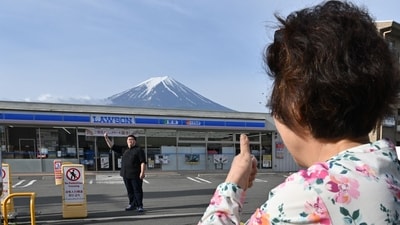 TOPSHOT - A person takes pictures of Mount Fuji from across the street of a convenience store, hours before the installation of a barrier to block the sight of Japan's Mount Fuji to deter badly behaved tourists, in the town of Fujikawaguchiko, Yamanashi prefecture on May 21, 2024. The plan to erect a large mesh barrier across the road from an Instagram-famous view of Mount Fuji made headlines last month when it was announced by officials fed up with what locals said were unending streams of mostly foreign visitors littering, trespassing and breaking traffic rules. (Photo by Kazuhiro NOGI / AFP) (AFP) TOPSHOT - A person takes pictures of Mount Fuji from across the street of a convenience store, hours before the installation of a barrier to block the sight of Japan's Mount Fuji to deter badly behaved tourists, in the town of Fujikawaguchiko, Yamanashi prefecture on May 21, 2024. The plan to erect a large mesh barrier across the road from an Instagram-famous view of Mount Fuji made headlines last month when it was announced by officials fed up with what locals said were unending streams of mostly foreign visitors littering, trespassing and breaking traffic rules. (Photo by Kazuhiro NOGI / AFP) (AFP)