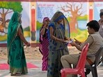 A woman shows her identity card and voter's slip to a policeman outside a polling station as she arrives to cast her vote in the sixth round of polling in Prayagraj on Saturday. 