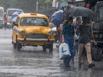 Commuters taking cover under umbrella cross road during rain, ahead of cyclone Remal�s landfall, in Kolkata, Sunday