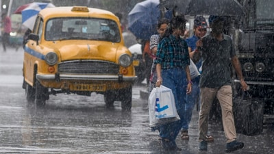 Commuters taking cover under umbrella cross road during rain, ahead of cyclone Remal�s landfall, in Kolkata, Sunday (PTI)