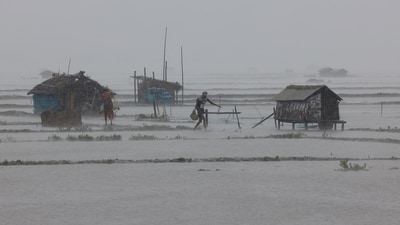 People walk along shrimp and crab farms that are flooded due to heavy rain as Cyclone Remal passes the country, in the Shyamnagar area of Satkhira, Bangladesh, May 27, 2024. (REUTERS)