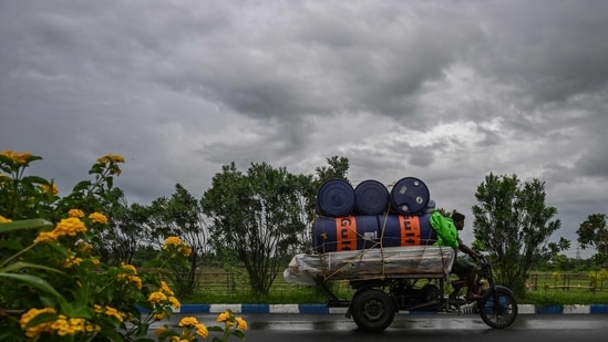 Workers drive their motorised three-wheeler along a road as rain clouds loom over the sky due to the effect of Cyclone Remal (AFP)