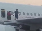 An IndiGo crew helping a passenger walk on the plane's wing after coming out of the emergency exit. An IndiGo crew helping a passenger walk on the plane's wing after coming out of the emergency exit.