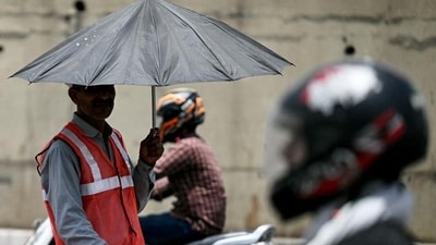 A toll booth worker (left) directing traffic takes shade under an umbrella on a hot summer afternoon in New Delhi on Wednesday. (AFP)