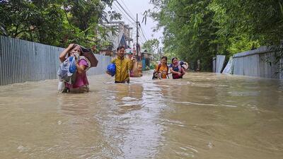 People carry their belongings through a flooded street following rains after the landfall of Cyclone Remal in Imphal on Wednesday. (PTI)