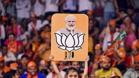 Stock market after Lok Sabha elections: A child holds a placard depicting PM Modi and BJP election symbol during a public meeting addressed by Uttar Pradesh Chief Minister Yogi Adityanath for Lok Sabha polls, in Varanasi. (PTI)