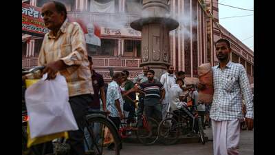 People stand below a water sprinkler installed on a pillar, to cool off, at a market place, amid heatwave in Varanasi on Friday (AFP)