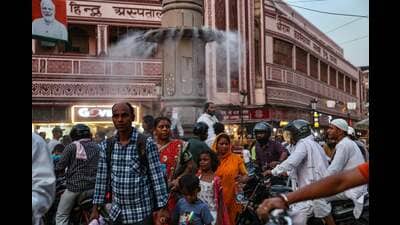 People walk past a water sprinkler installed on a pillar at a market place, amid heatwave in Varanasi. (AFP.)