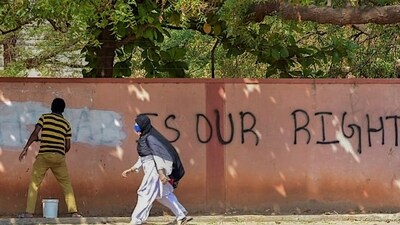 A hijab-wearing student walks past a worker painting a wall to conceal a pro-hijab slogan written on the wall. Representational Photo.. (PTI Photo) A hijab-wearing student walks past a worker painting a wall to conceal a pro-hijab slogan written on the wall. Representational Photo.. (PTI Photo)
