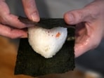 A person wraps seaweed around a rice ball to make onigiri. The humble sticky-rice ball, a mainstay of Japanese food, has entered the global lexicon. (AP)