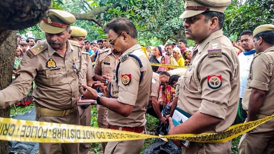 Police personnel investigate after the bodies of two girls were found hanging from a tree, at Kayamganj area in Farrukhabad on August 27, 2024. (PTI)